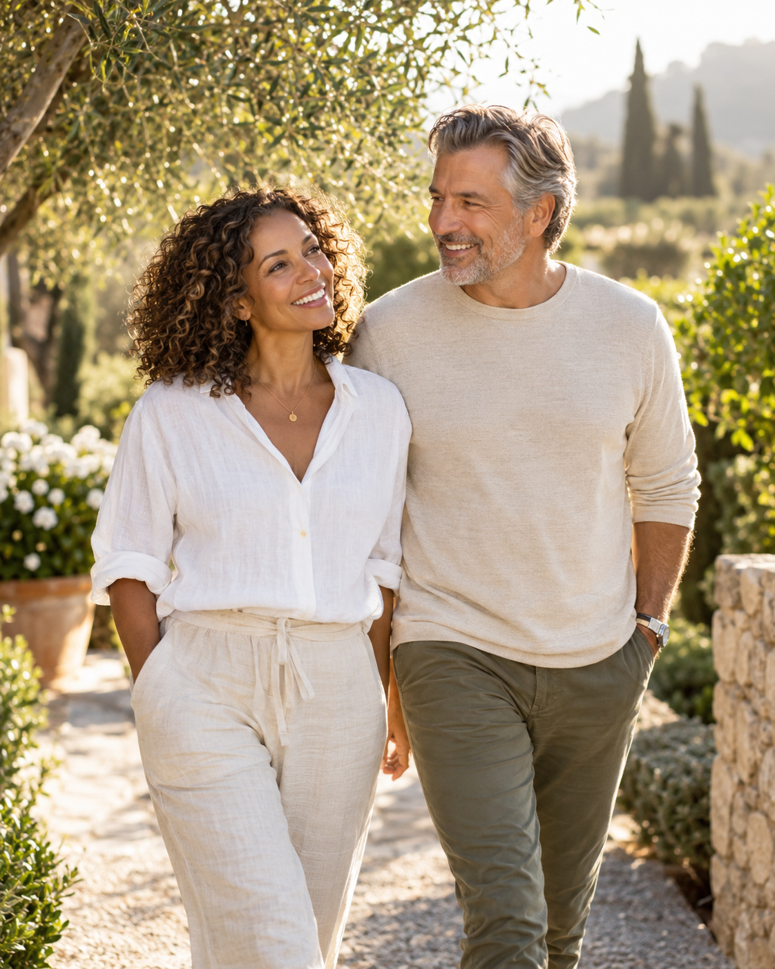 A smiling mature couple walking along a sunlit garden path.
